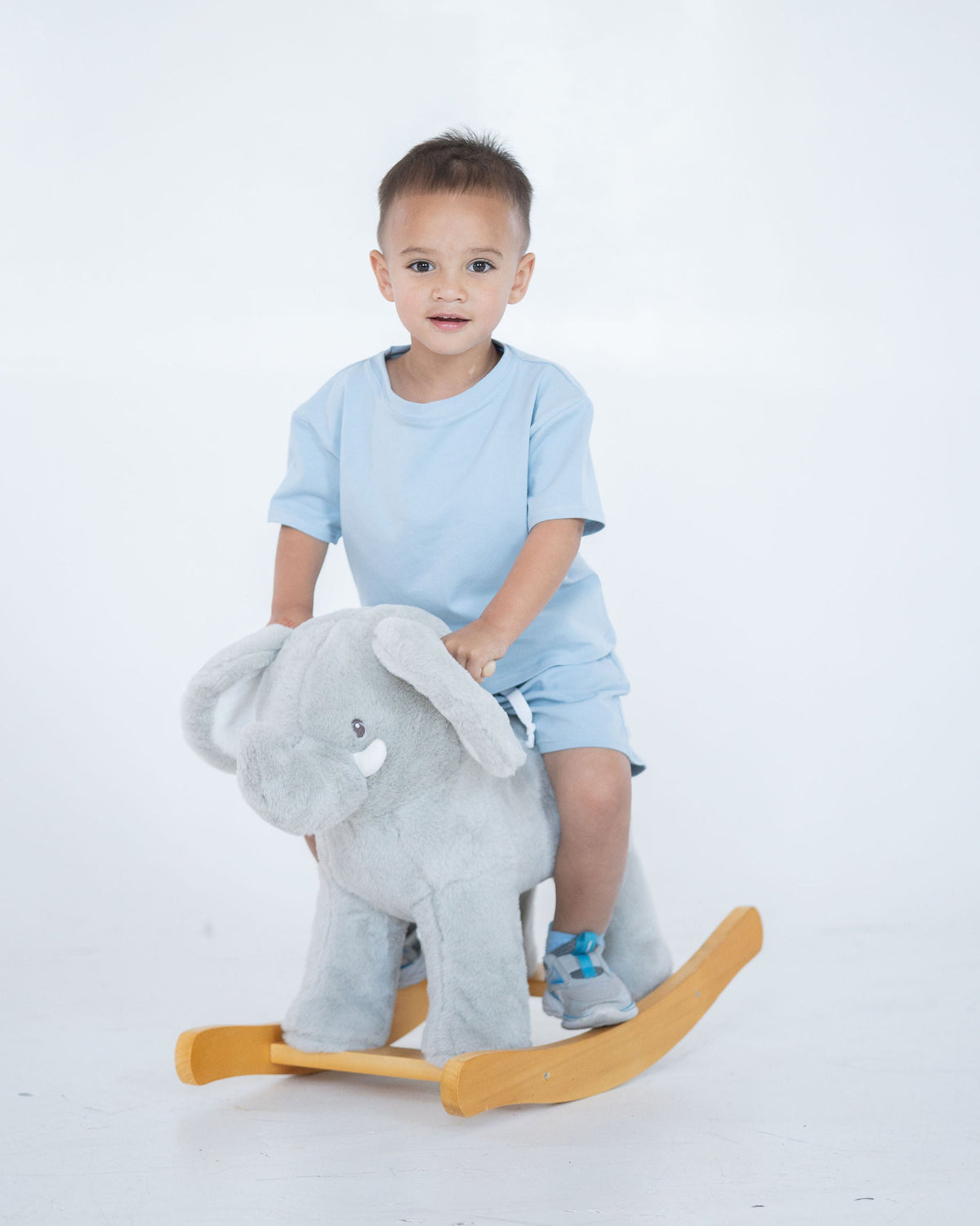 Child sitting on a gray elephant rocking horse against a white background