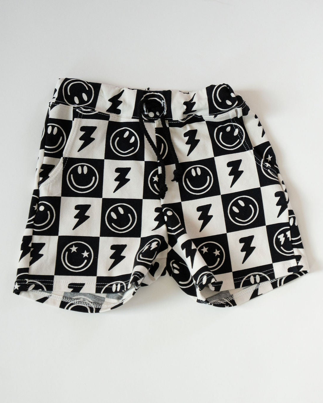 Black and white checkered shorts with smiley face and lightning bolt pattern on a white background