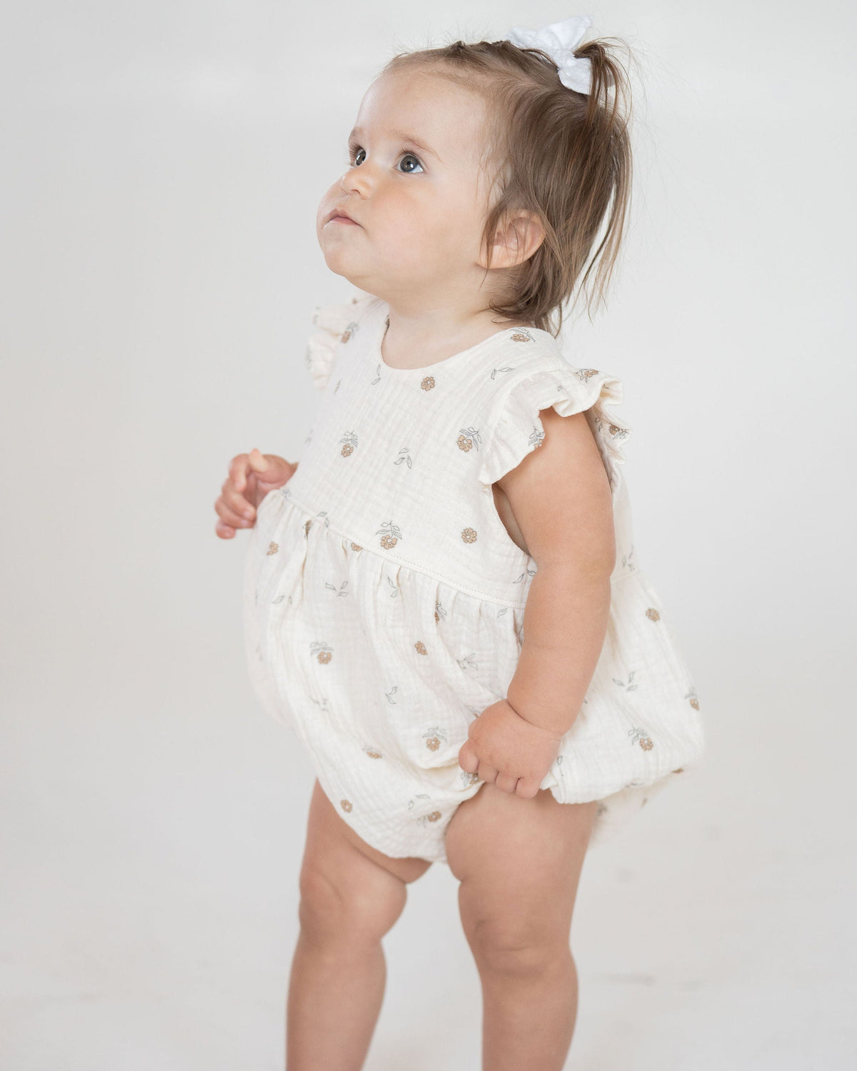 Baby wearing a white ruffled romper on a plain background
