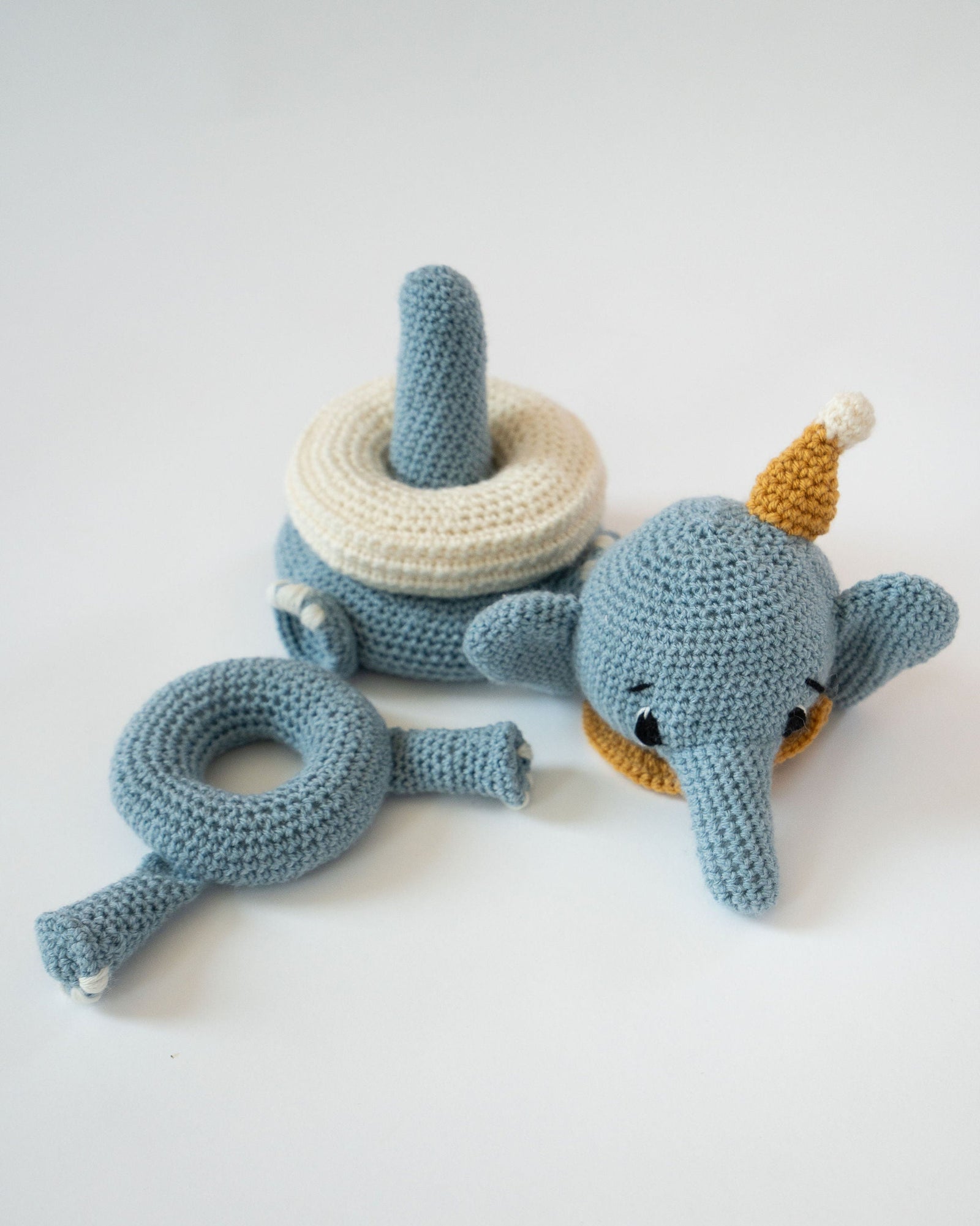 Crocheted elephant toy with a yellow hat on a white background