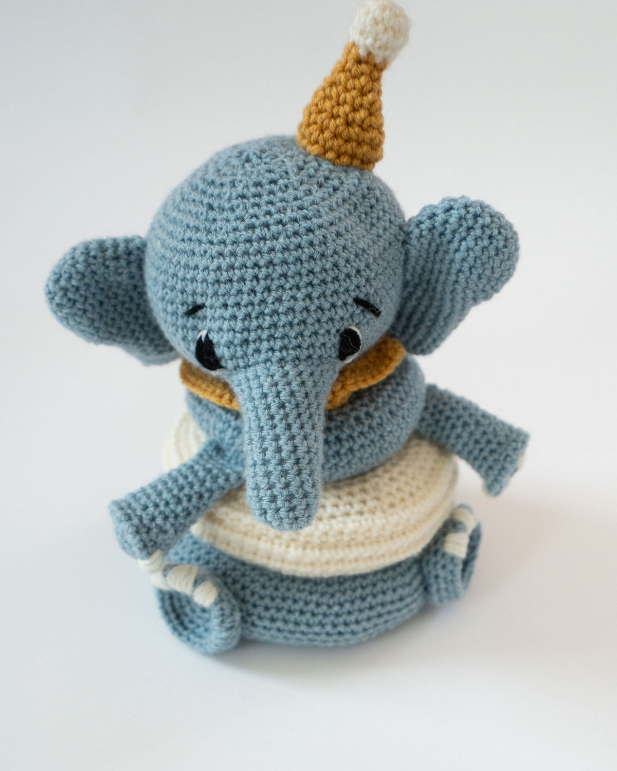 Crocheted elephant toy with a yellow hat on a white background