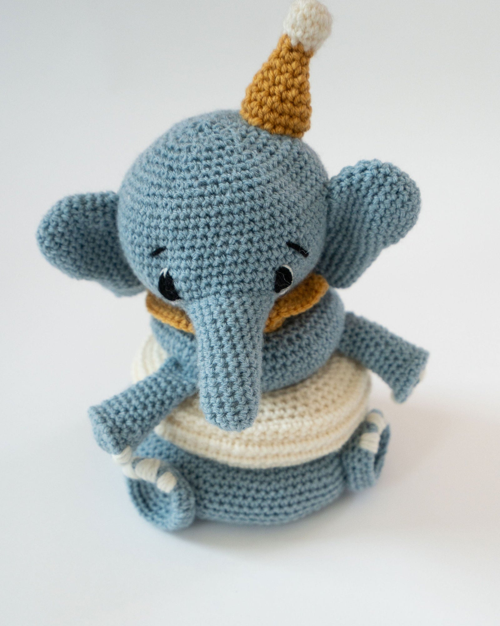 Crocheted elephant toy with a yellow hat on a white background