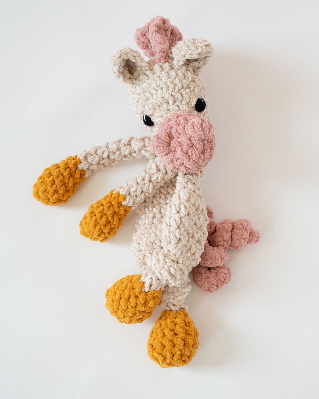Crocheted giraffe toy with pink and yellow accents on a white background