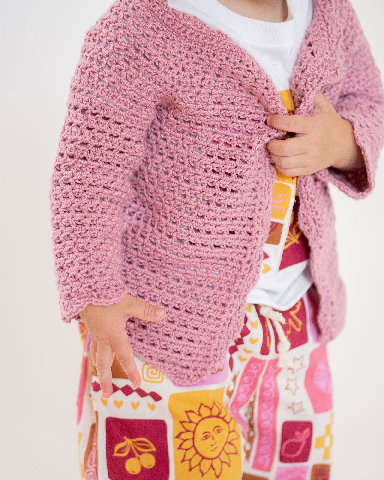 Pink crocheted baby cardigan on a white background