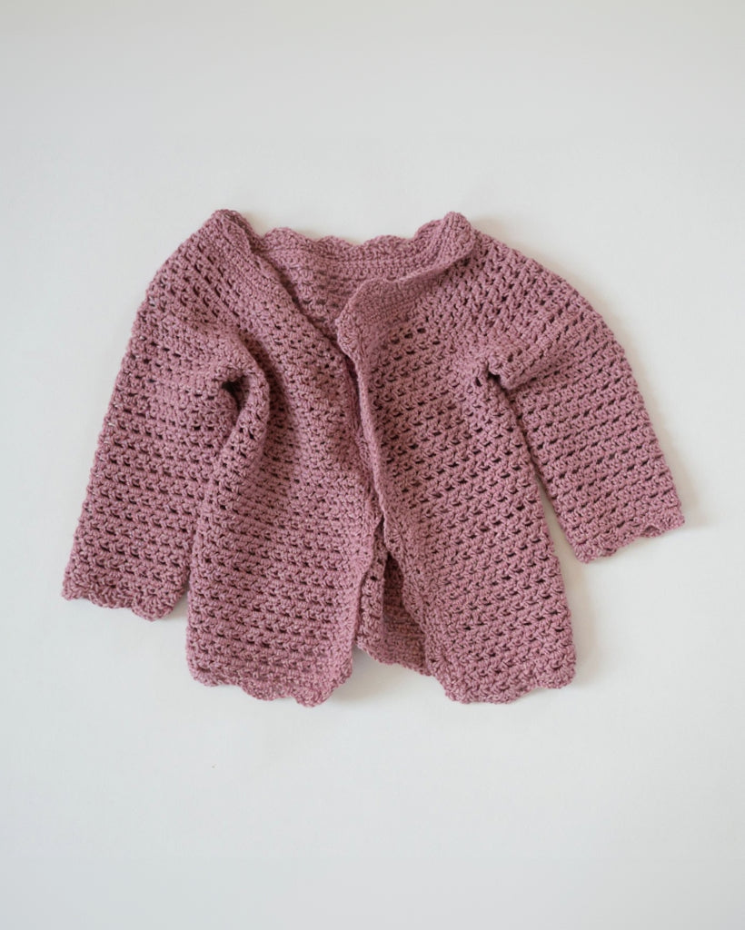 Pink crocheted baby cardigan on a white background