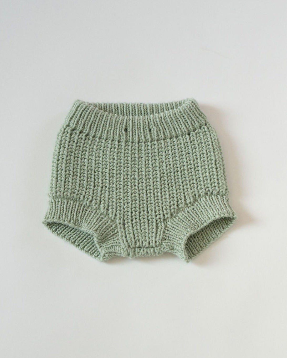 Knitted green baby bloomers on a light gray background