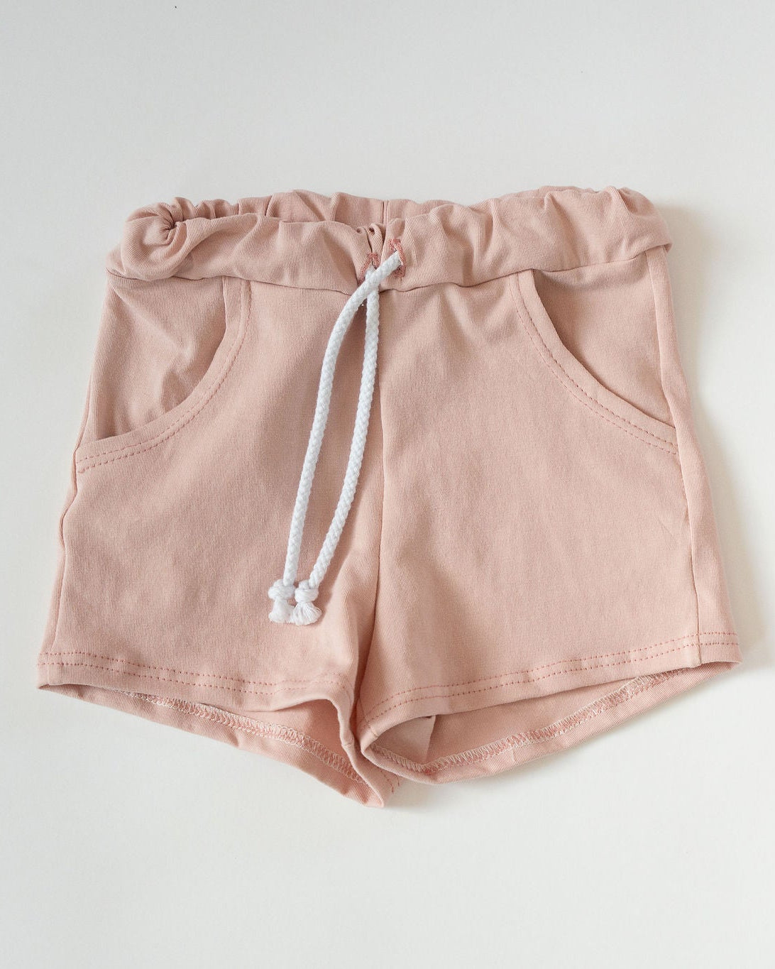 Pink shorts with a white drawstring on a light gray background