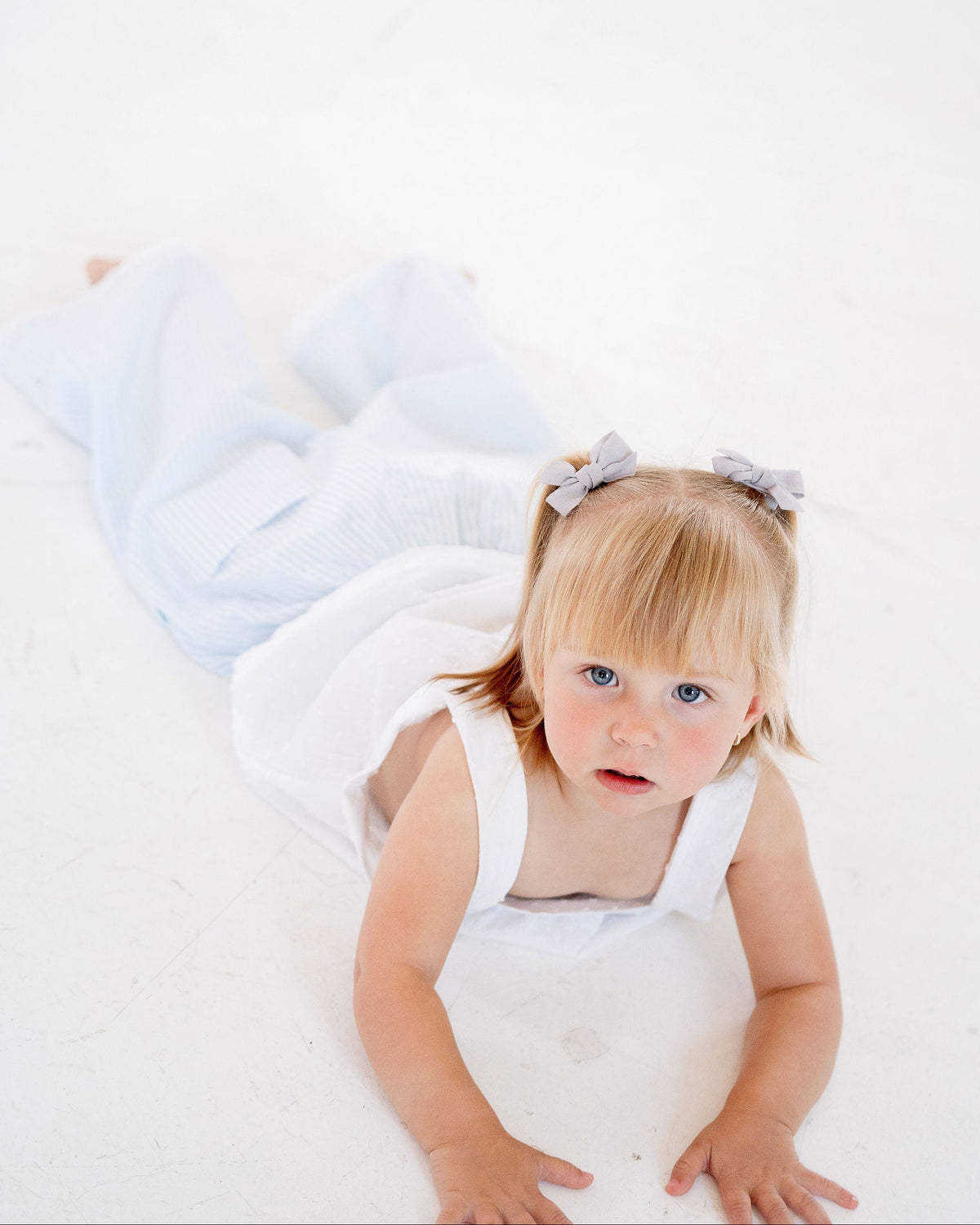 Young child wearing a white dress with a bow on a white background