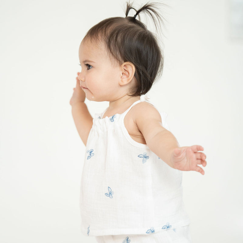 Baby in a white dress with blue patterns on a plain background