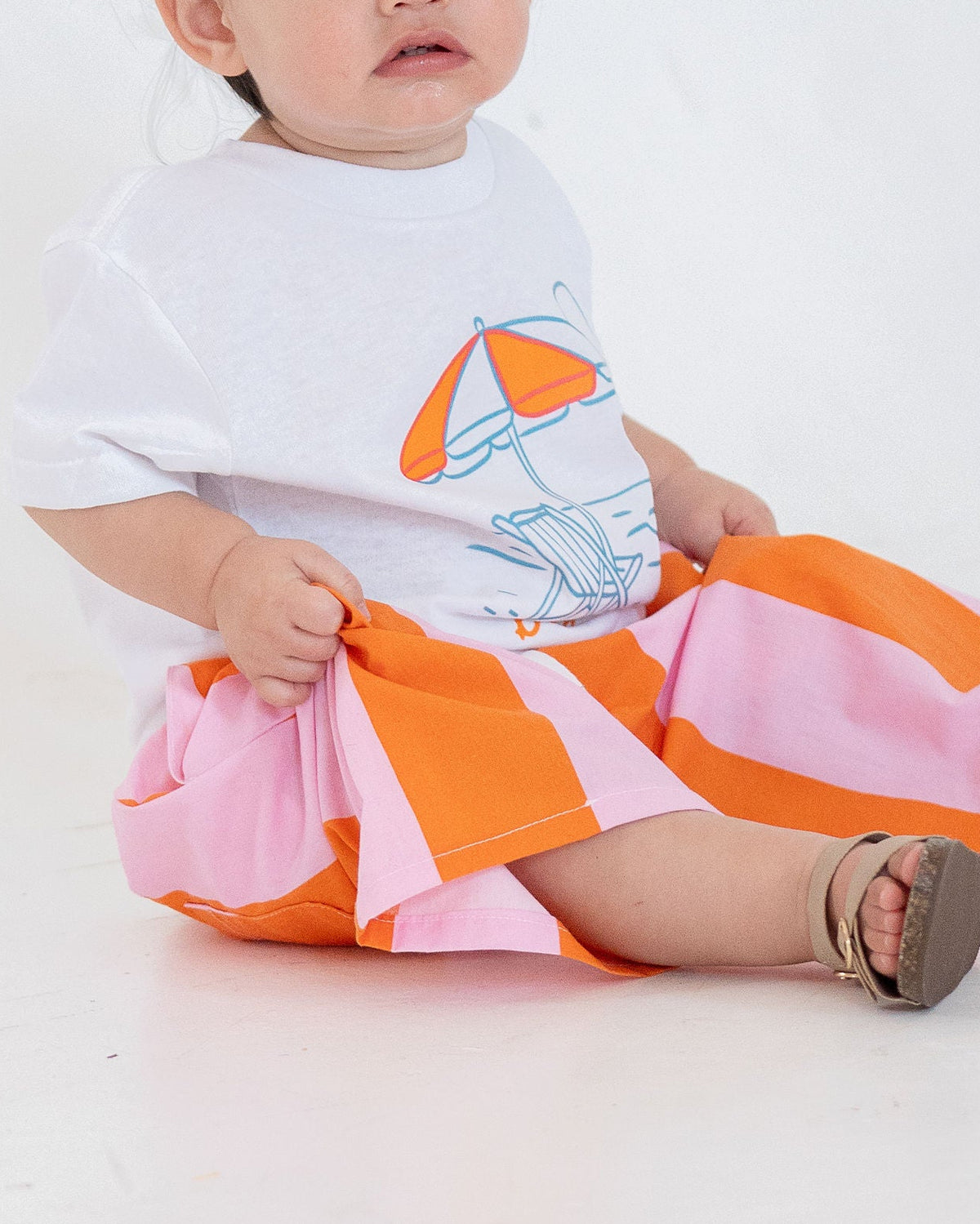 Baby wearing a white shirt with a cartoon design and colorful pants on a white background