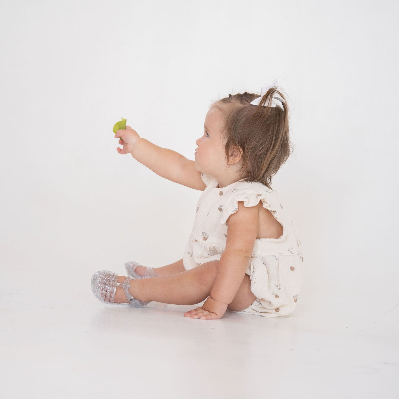 Baby sitting on a white floor holding a green toy
