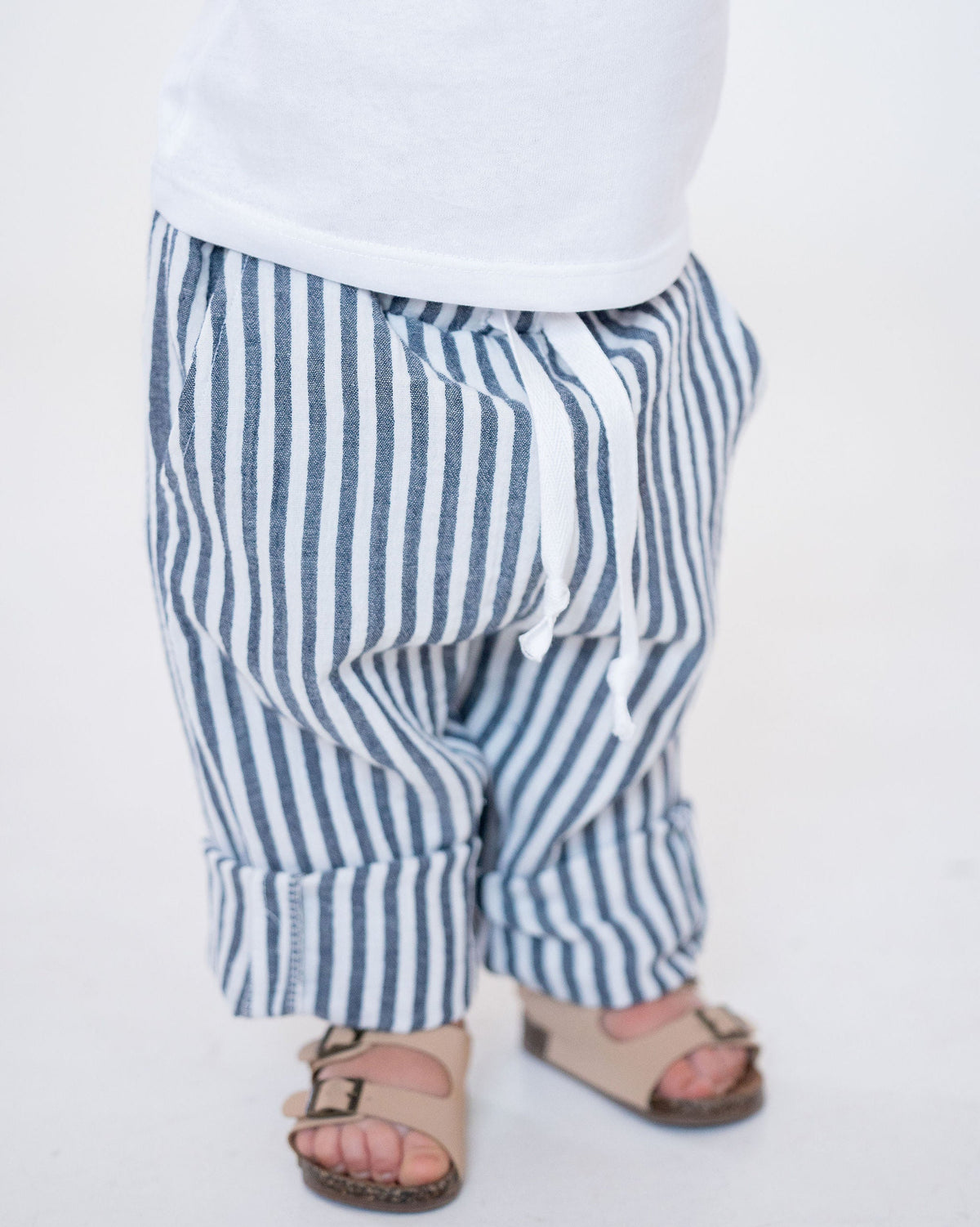 Child wearing a white shirt with a blue truck design and striped blue and white pants on a white background