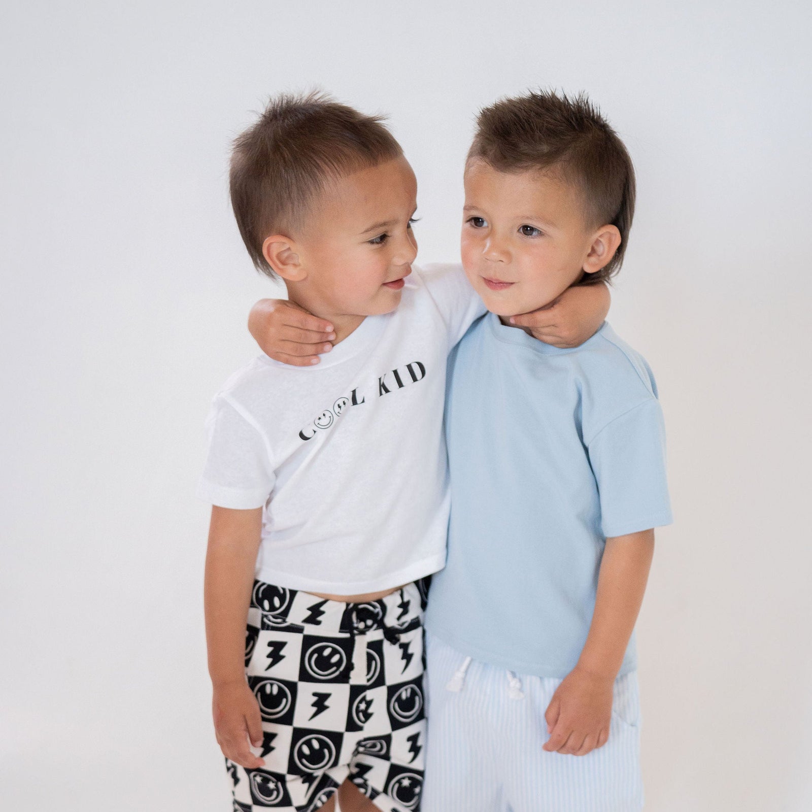 Two young boys standing close together wearing matching outfits on a white background