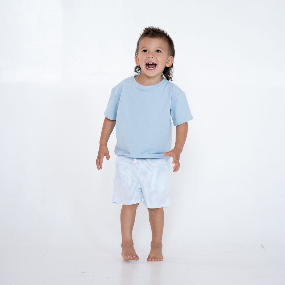Child wearing a light blue shirt and shorts on a white background