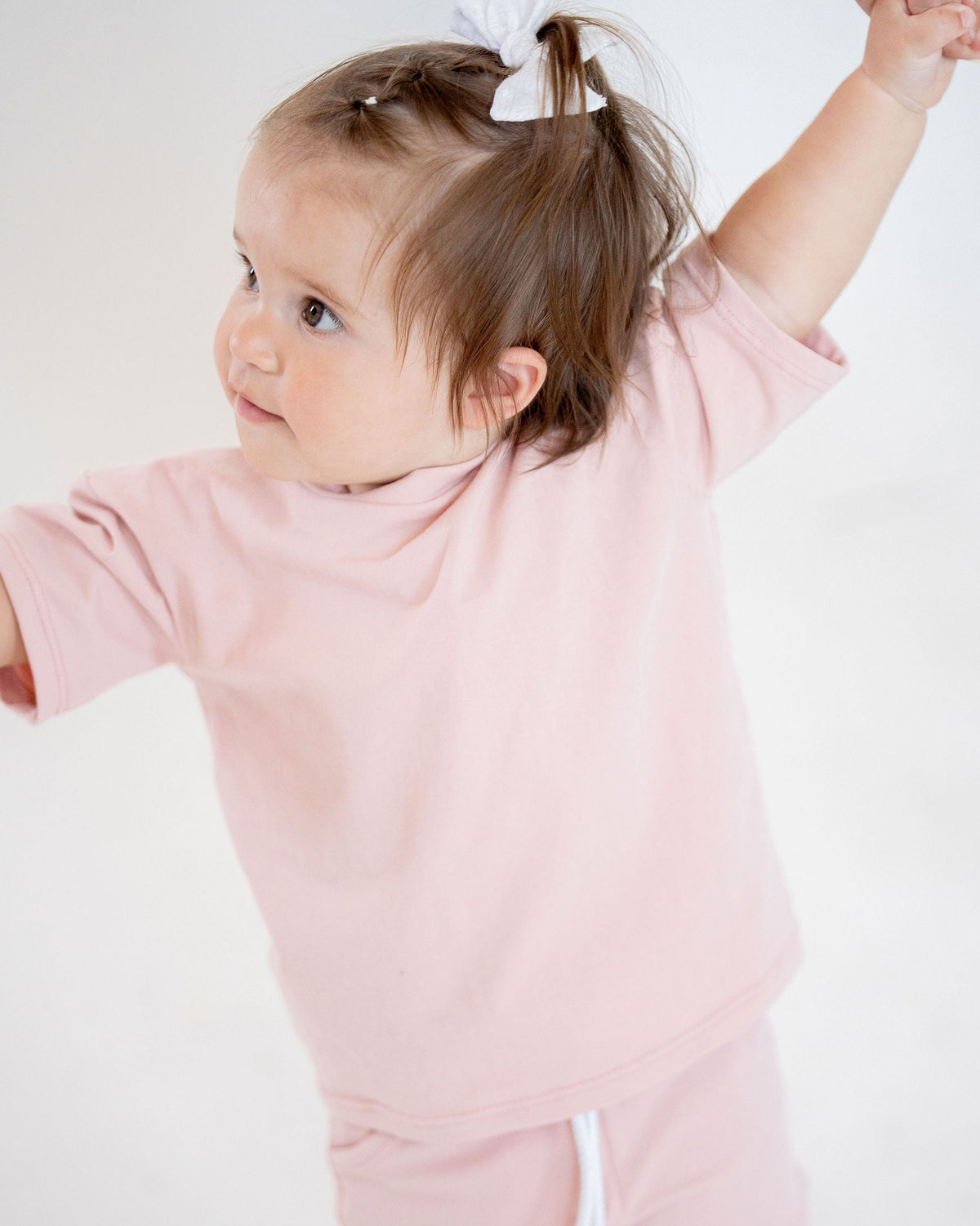 Child wearing a pink dress with white drawstrings on a plain background