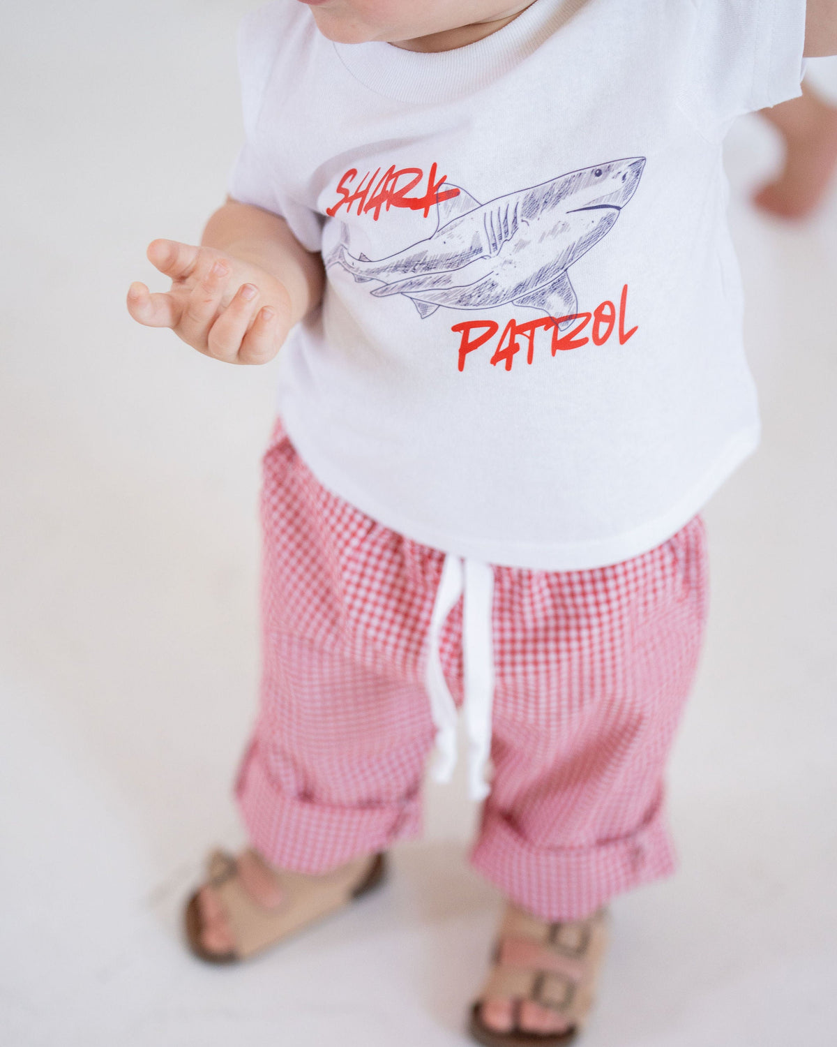 Child wearing a white shirt with a shark design and text, standing on a light background