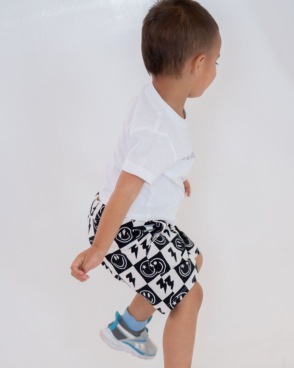 Child wearing a white t-shirt and black and white patterned shorts on a white background