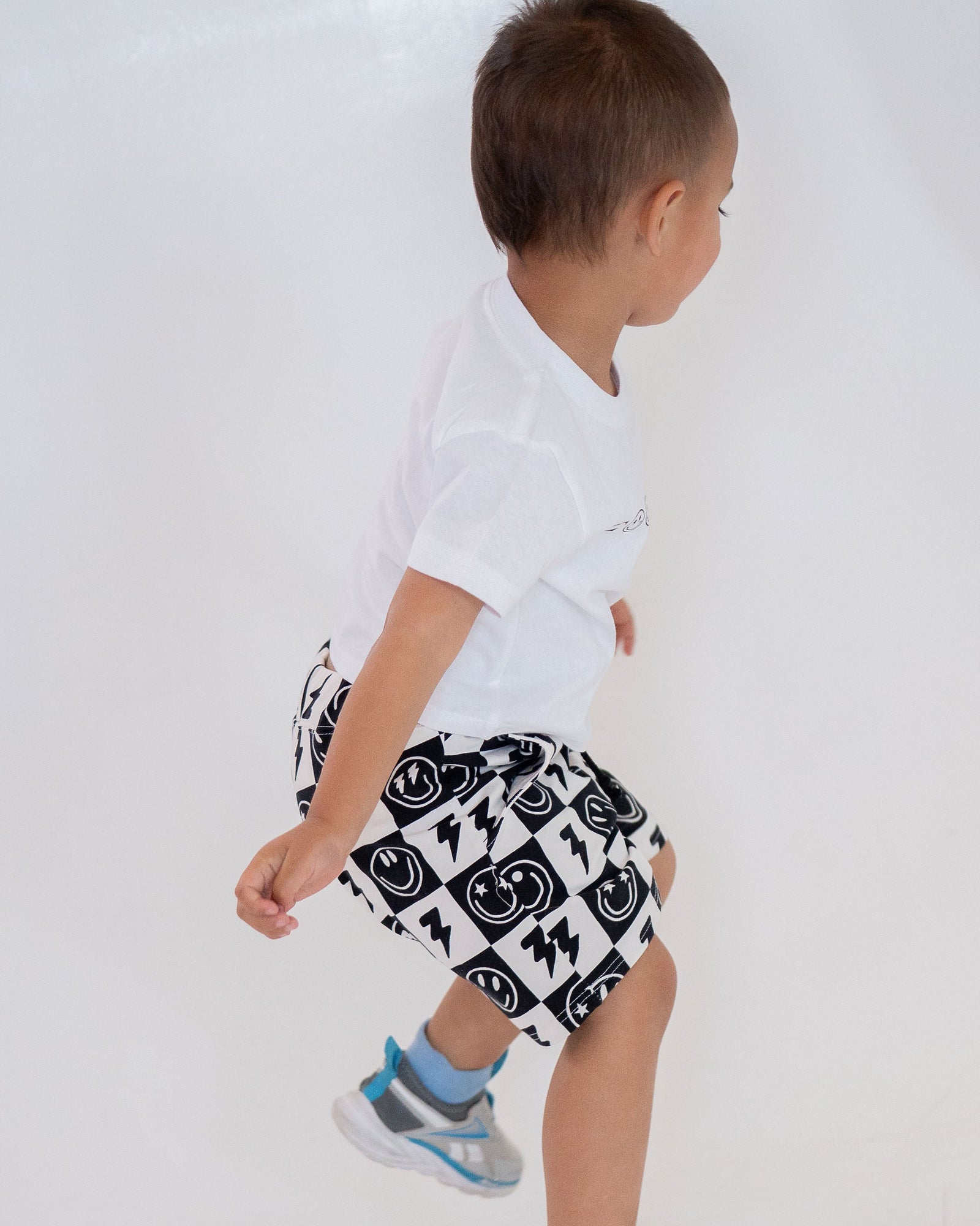 Black and white checkered shorts with smiley face and lightning bolt pattern on a white background