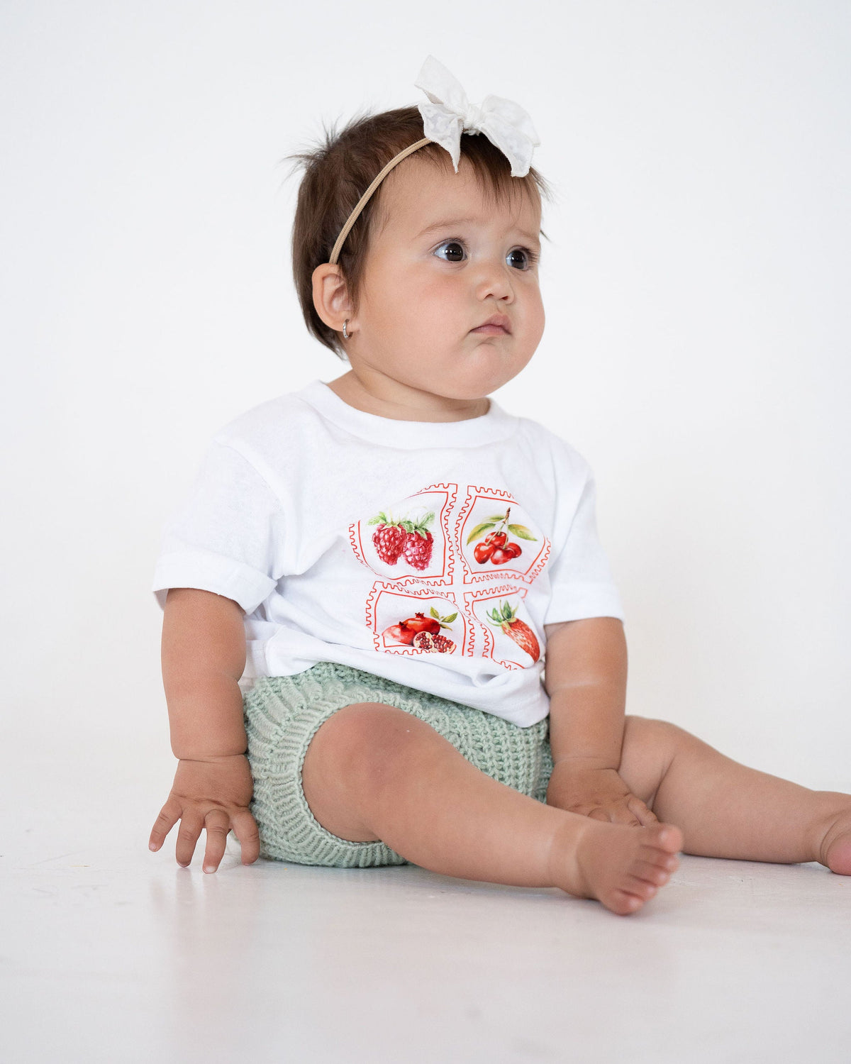 Baby wearing a white shirt with red graphics and green shorts on a white background