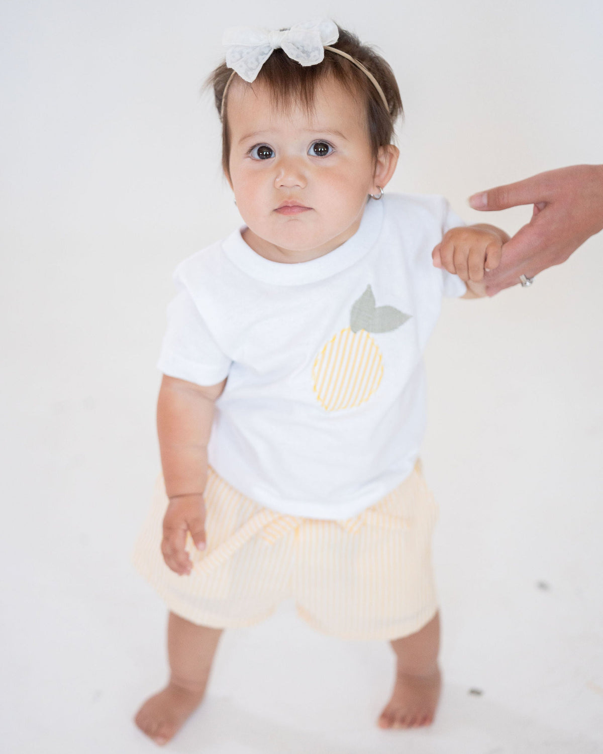 Baby wearing a white onesie with a pineapple design on a white background